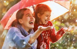 Mother and daughter under an umbrella, sheltering on a sunny but rainy day.